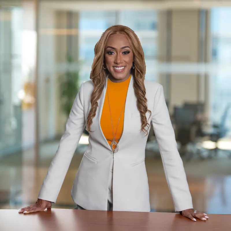 Dr. Wendy Ellis Jones, the NIL Doctor, is standing at a table smiling. Wendy is wearing an orange shirt and white blazer, and has brown hair. Wendy offers speaking engagements and NIL services all across the nation. Let Wendy serve as your trusted motivational speaker or NIL consultant.
