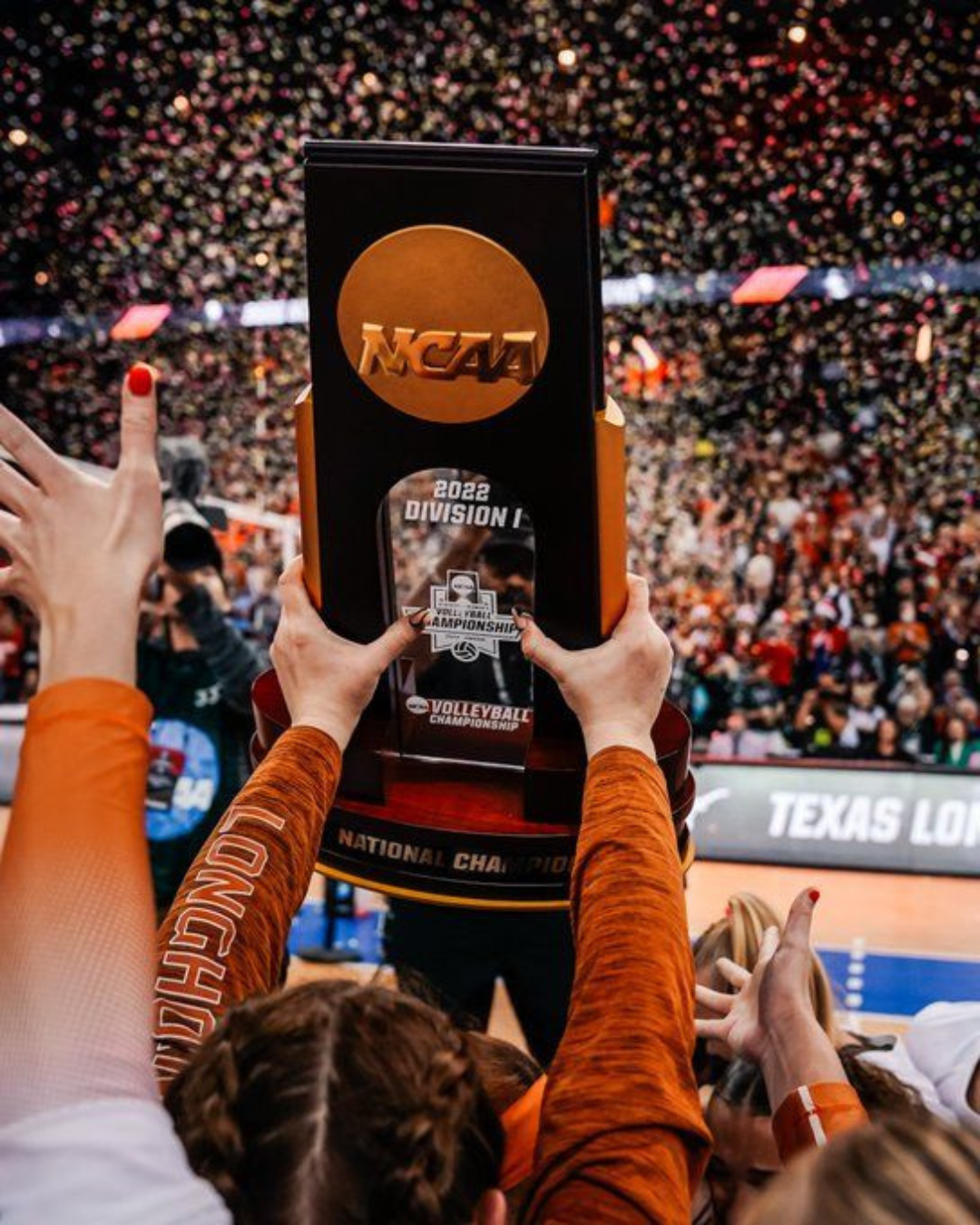 A fan of the Texas Longhorns holds up a National Collegiate Athletic Association trophy in front of a basketball court.